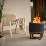 Aurus low-smoke fire pit lit beside a woven armchair on a covered patio